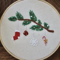 A close up of the hand embroidered branch with a stocking, ornament, snowflake, and candy cane