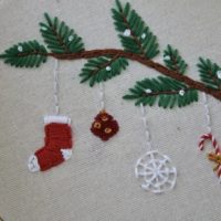 A close up of the hand embroidered branch with a stocking, ornament, snowflake, and candy cane