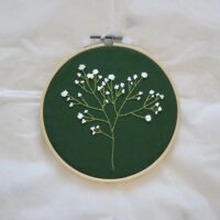 A 6 inch embroidery hoop with a forest green material hand embroidered with an intricate Gypsophila / baby's breath flower sprig