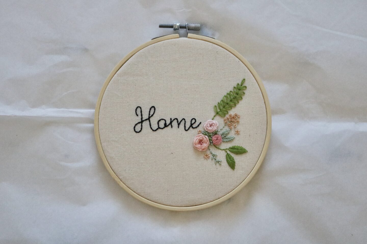A 6 inch embroidery hoop hand embroidered with a floral motif and handwritten text reading 'Home'
