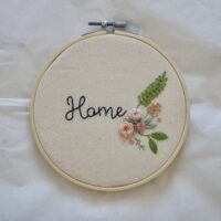 A 6 inch embroidery hoop hand embroidered with a floral motif and handwritten text reading 'Home'