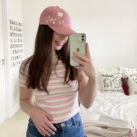 brunette model taking a mirror selfie wearing the pink floral cap