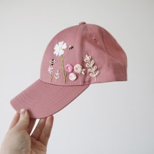 pink cap hand embroidered with a big white flower, daisy, pink roses, green leaves and vines, and bees