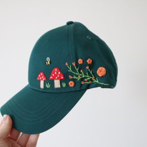 forest green cap hand embroidered with toadstools, bees, and green vines with orange roses