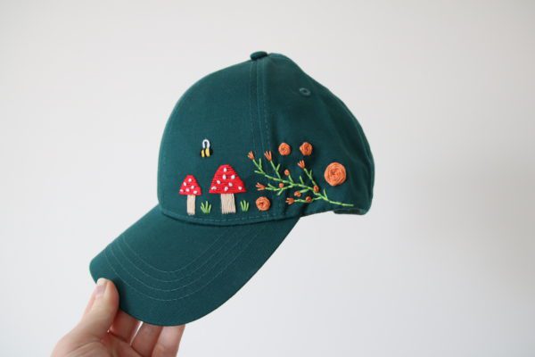 forest green cap hand embroidered with toadstools, bees, and green vines with orange roses