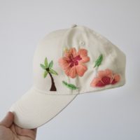 overview of a cream cap with a palm tree and hibiscus flower