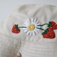 close up of hand embroidered daisy and 3 red strawberries
