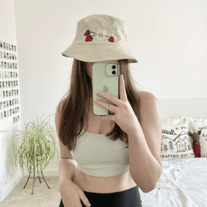 brunette model taking a mirror selfie wearing the cream bucket hat with hand embroidered strawberries and a daisy