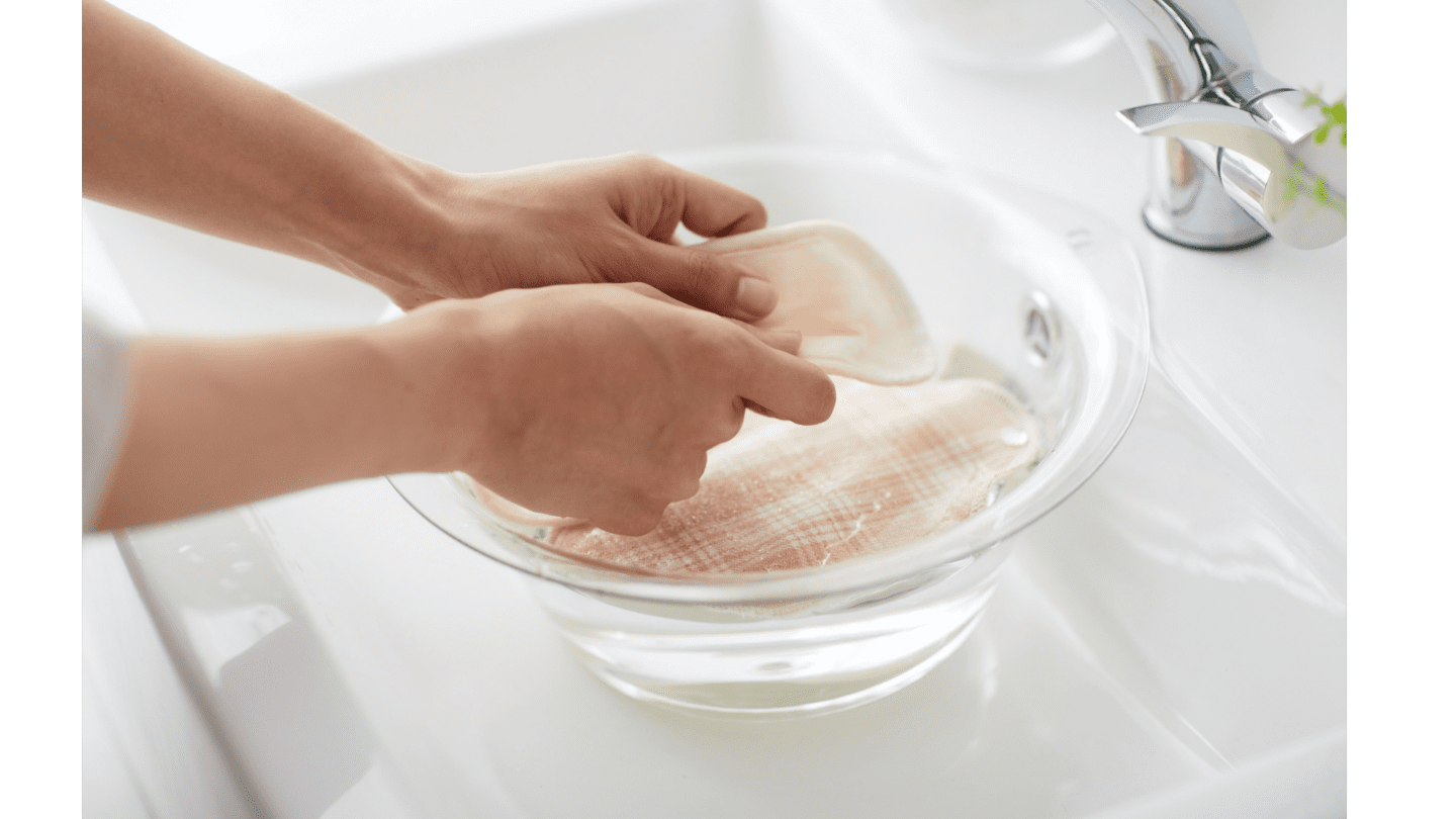 A pair of hands hand washing clothing in a sink