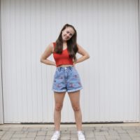 full body image of a brunette girl wearing denim shorts embroidered with strawberries and a red top