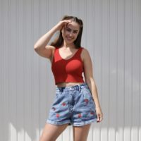 brunette model wearing blue denim shorts hand embroidered with strawberries and a red top