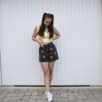 brunette girl wearing black shorts embroidered with sunflowers and a yellow top