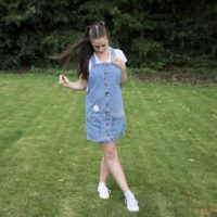 brunette girl wearing a denim pinafore dress hand embroidered with pink flowers and bees