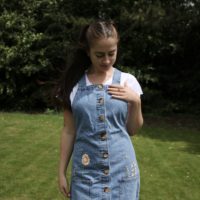 close up of the girl wearing a blue denim pinafore dress hand embroidered with pink flowers, greenery, and bees