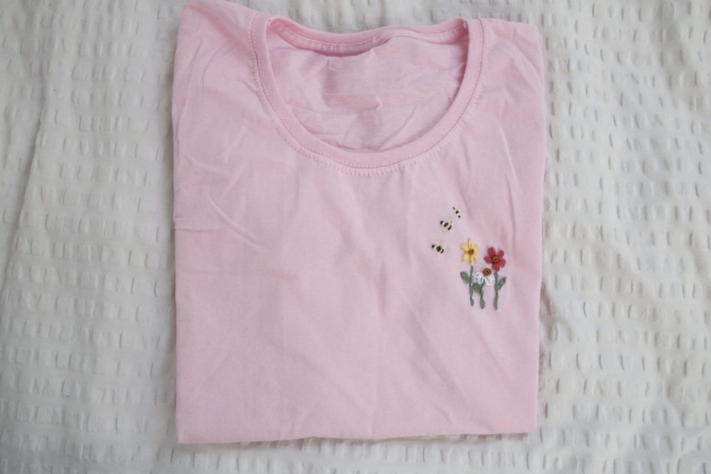 a pink t-shirt hand embroidered with 2 flowers and 3 bees