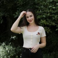 brunette girl wearing cream crop top hand embroidered with a butterfly and flowers