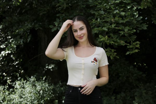 brunette girl wearing cream crop top hand embroidered with a butterfly and flowers