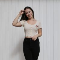 brunette girl wearing cream crop top hand embroidered with a butterfly and flowers