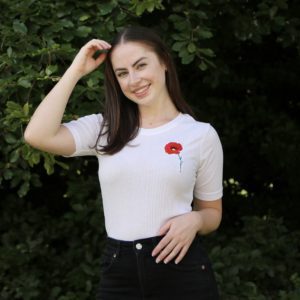 brunette girl wearing a white top hand embroidered with a red poppy