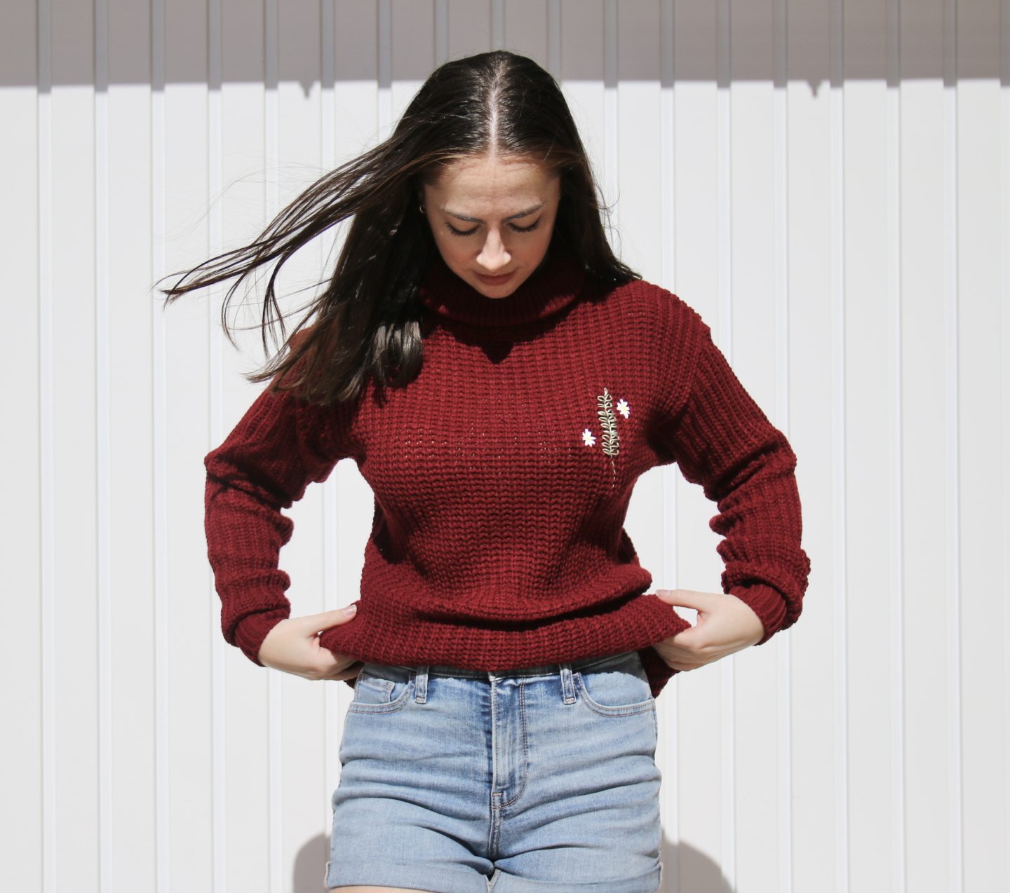 brunette girl wearing a red jumper hand embroidered with a rosemary sprig and daisies