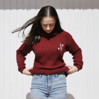 brunette girl wearing a red jumper hand embroidered with a rosemary sprig and daisies
