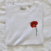 white top hand embroidered with a detailed poppy on the left breast