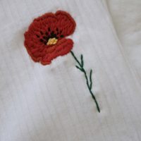 Close up of stitch work of a hand embroidered red poppy on a white t-shirt