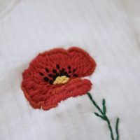 a close up of stitch work of a hand embroidered red poppy.