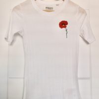 A long white t-shirt hung up, hand embroidered with a red poppy on the left breast