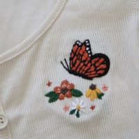 Close up of an embroidered orange monarch butterfly and orange, yellow and white flowers