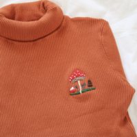 close up of embroidered mushrooms on an orange jumper