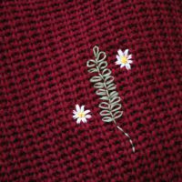 Close up of the stitch work on embroidered rosemary and daisies