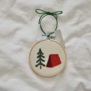 A 3 inch embroidery hoop hand embroidered with a red tent and tree