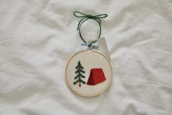 A 3 inch embroidery hoop hand embroidered with a red tent and tree
