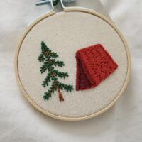 A close up of a hand embroidered red tent and tree