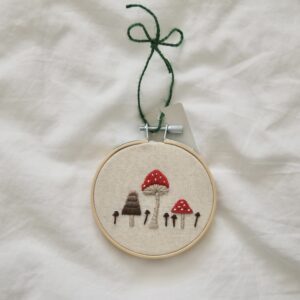 A 3 inch hoop hand embroidered with a red toadstool mushroom and fungi
