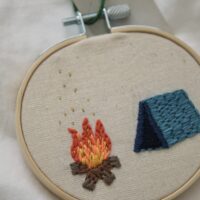 close up of hand embroidered blue tent and a campfire with metallic gold flakes