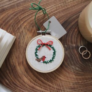 A 3 inch Christmas tree decoration hand embroidered with a wreath, red ribbon and a robin