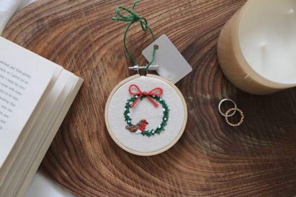 A 3 inch Christmas tree decoration hand embroidered with a wreath, red ribbon and a robin