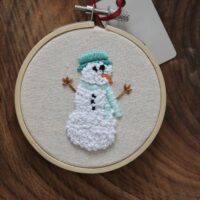 Close up of a hand embroidered snowman wearing a blue hat and scarf