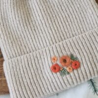 close up of hand embroidered orange roses on a cream beanie