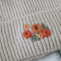 Close up of hand embroidered orange roses on a cream beanie