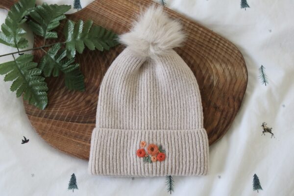 Cream pom pom beanie hand embroidered with orange roses and green leaves