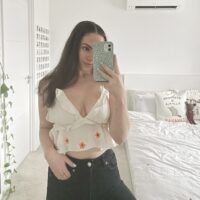 Brunette girl taking a mirror selfie wearing a floaty white crop top hand embroidered with pink cherry blossom