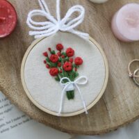 Hand embroidery red roses in a bouquet, tied with string, framed in a 3 inch wooden hoop.