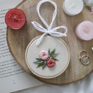 a 3 inch embroidery hoop hand tied with white ribbon. It is hand embroidered with 2 pink roses and green leaves