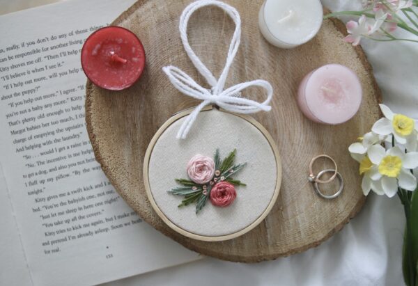 a 3 inch embroidery hoop hand tied with white ribbon. It is hand embroidered with 2 pink roses and green leaves
