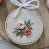 a 3 inch embroidery hoop hand stitched with 2 pink roses and green leaves
