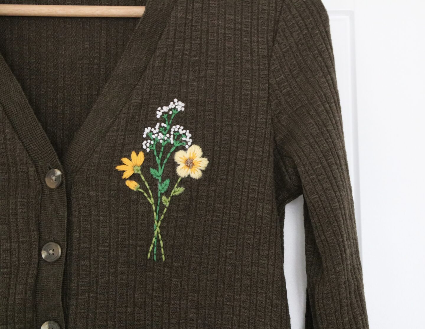 Khaki cardigan hand embroidered with a bouquet of flowers featuring; gypsophila, blanket flowers, and cosmos.