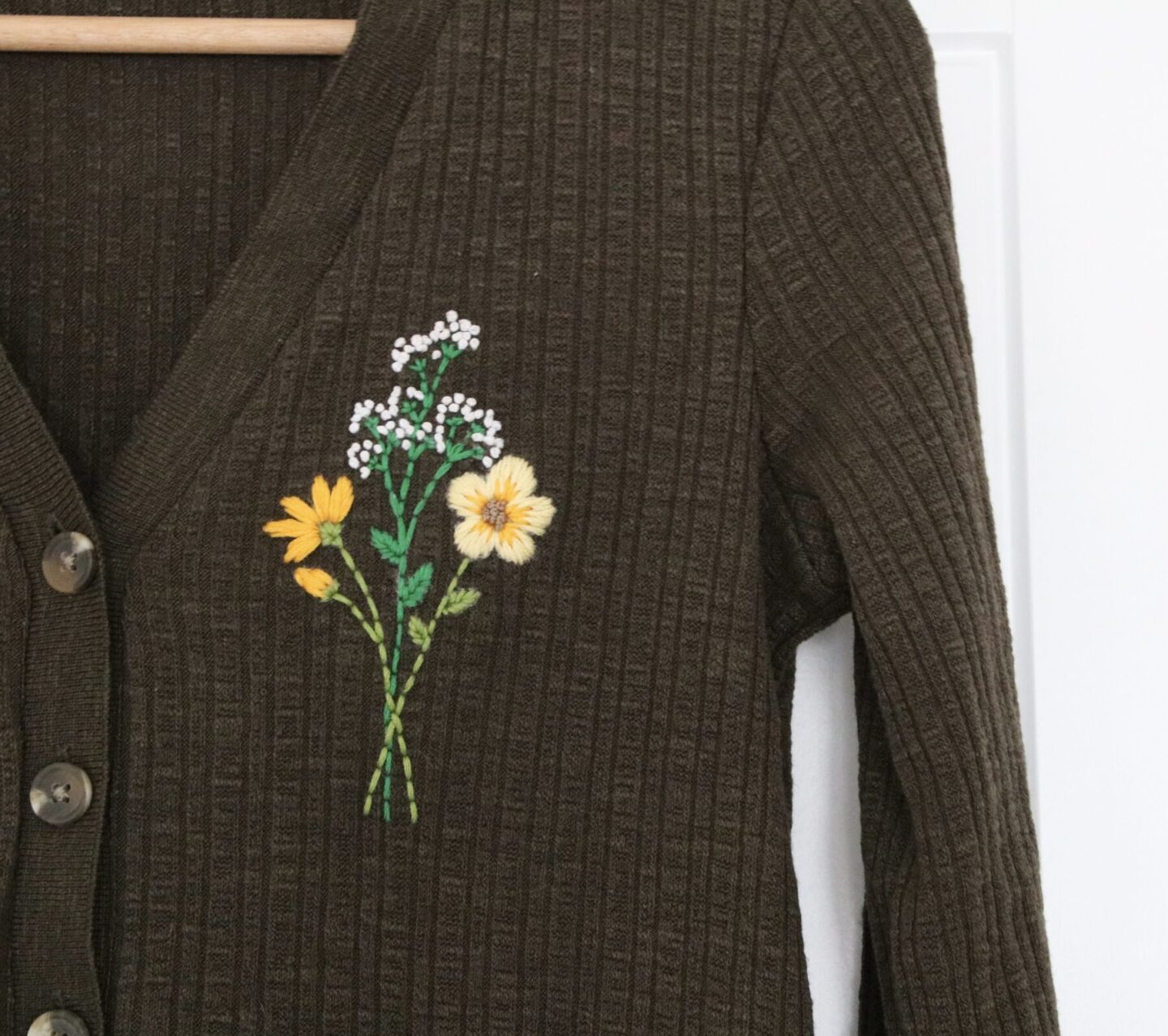 Khaki cardigan hand embroidered with a bouquet of flowers featuring; gypsophila, blanket flowers, and cosmos.